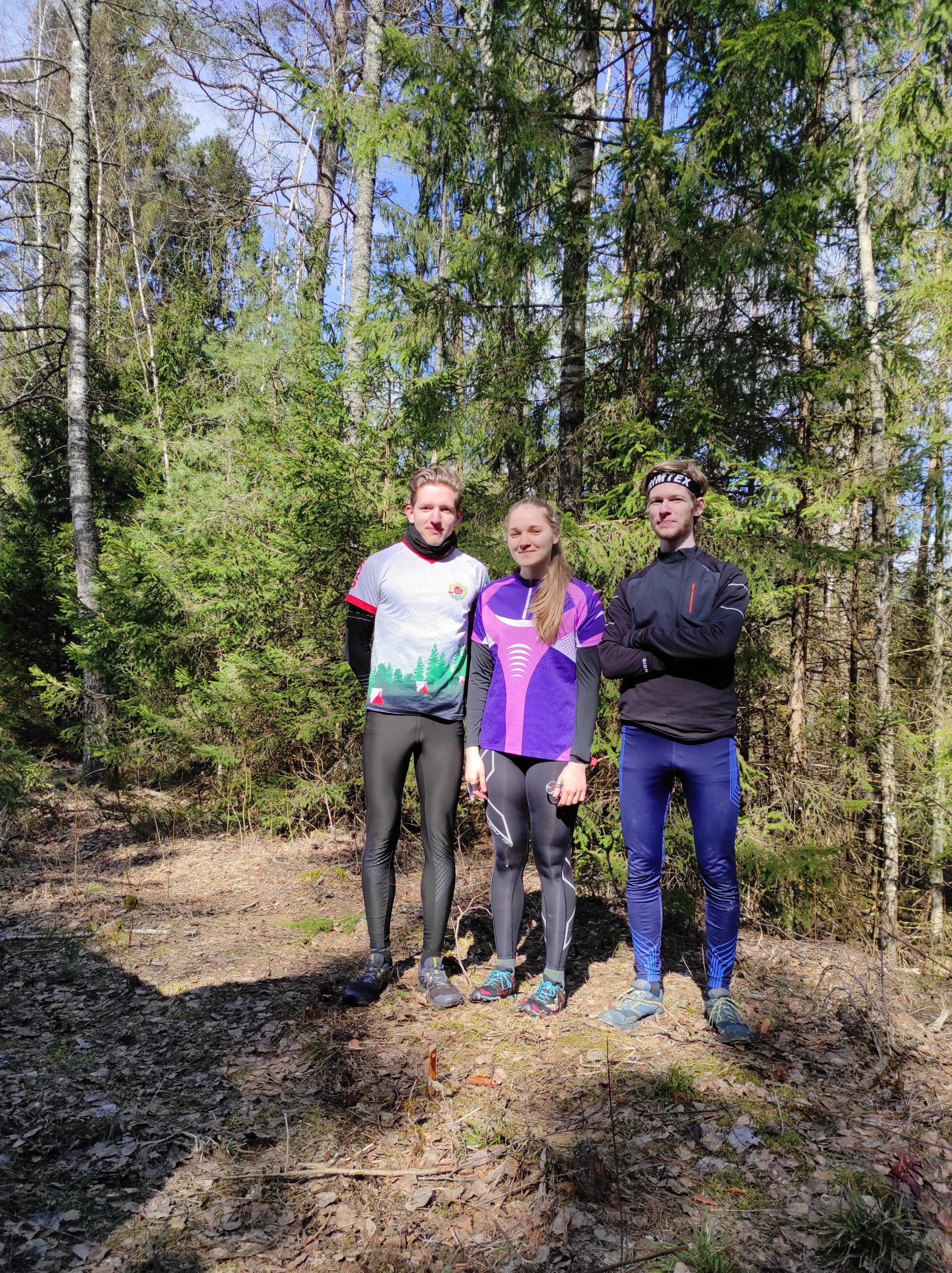 Du studentai ir viena studentė stovi miške