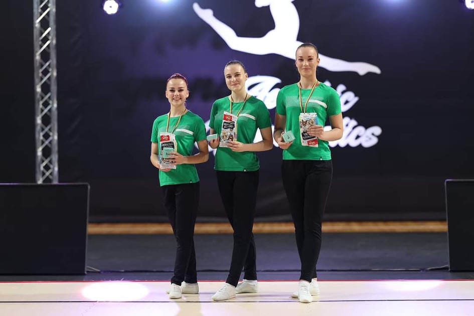 Trys merginios, vilkinčios žalios spalvos marškinėlius, stovi ant scenos