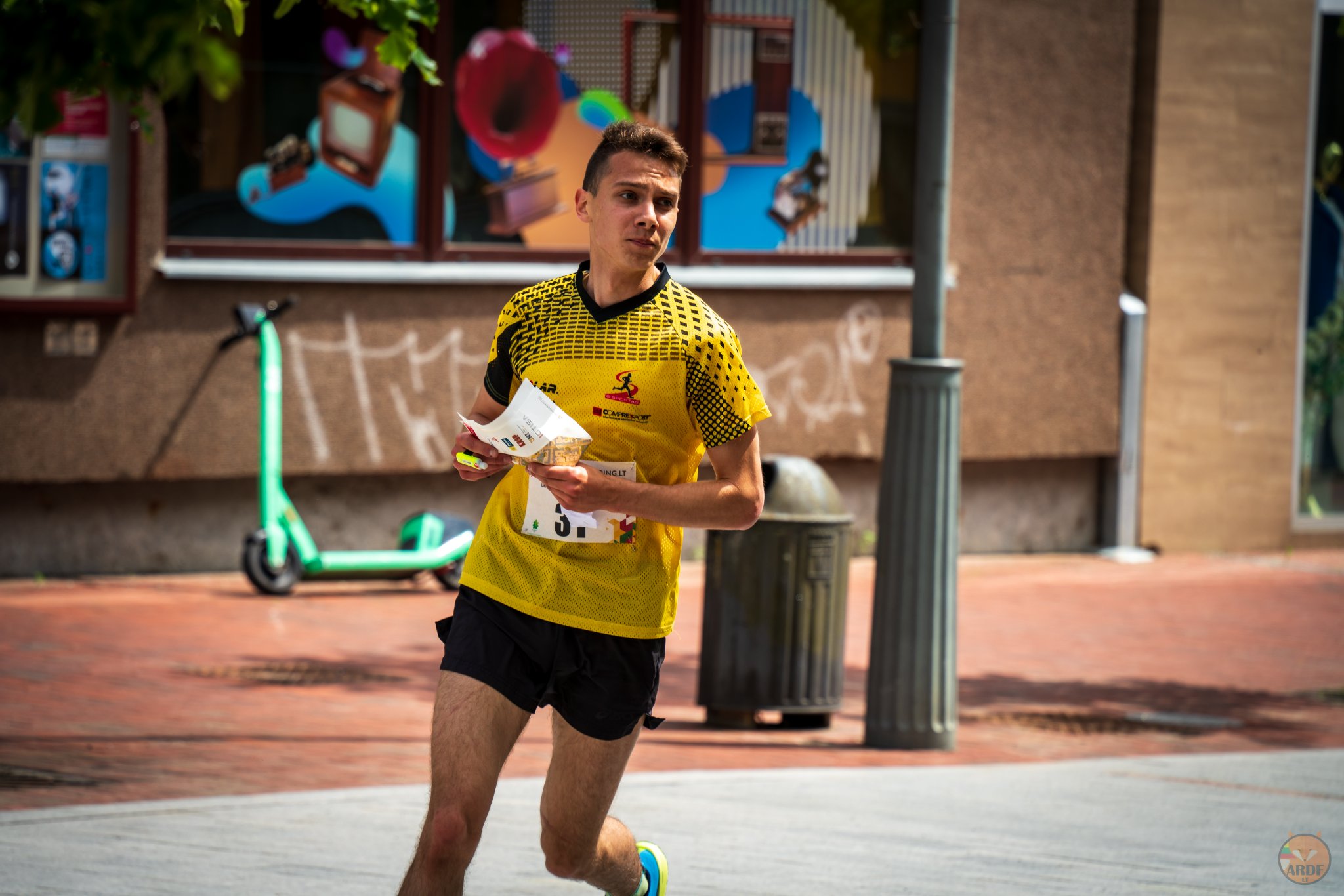 Vaikinas, dėvintis geltonus marškinėlius, bėga rankose laikydamas popieriaus lapą