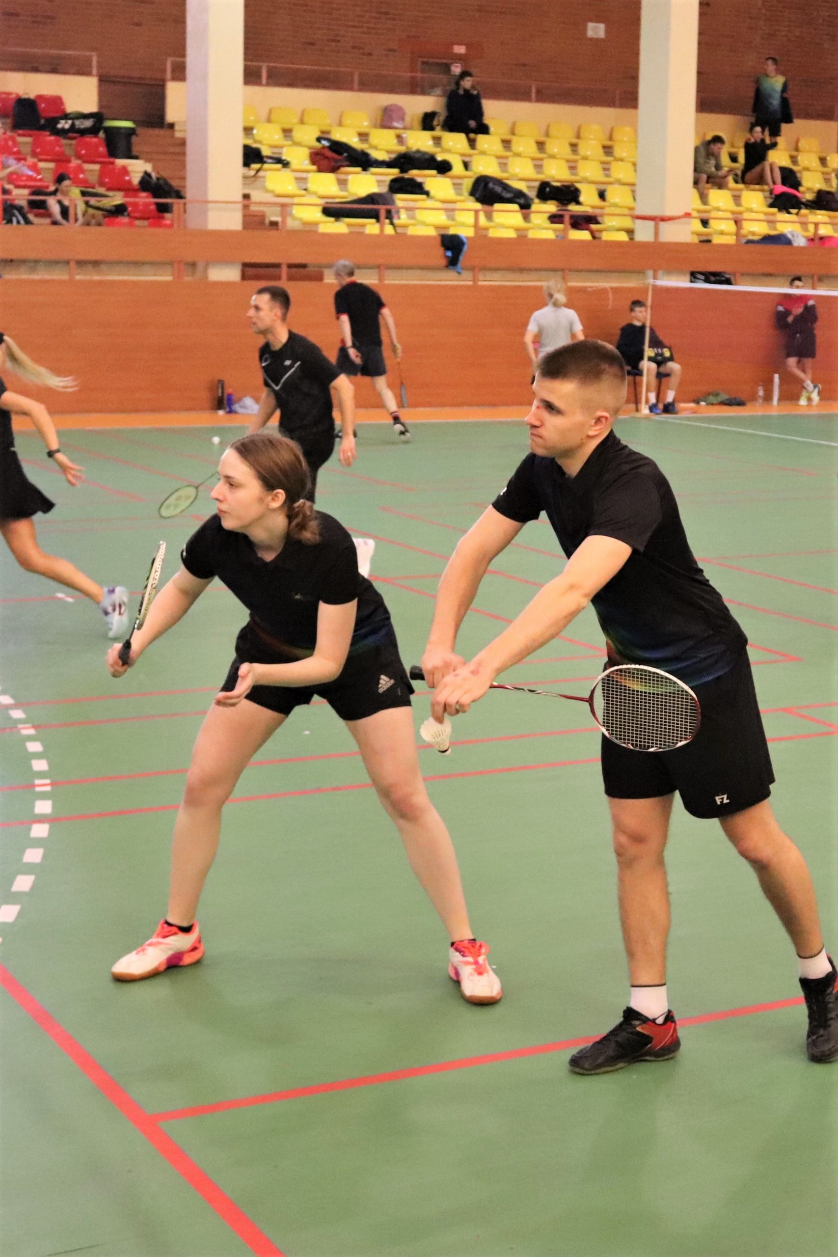 Du studentai - vaikinas ir mergina juoda sportine apranga, žaidžia badmintoną badmintono aikštelėje.