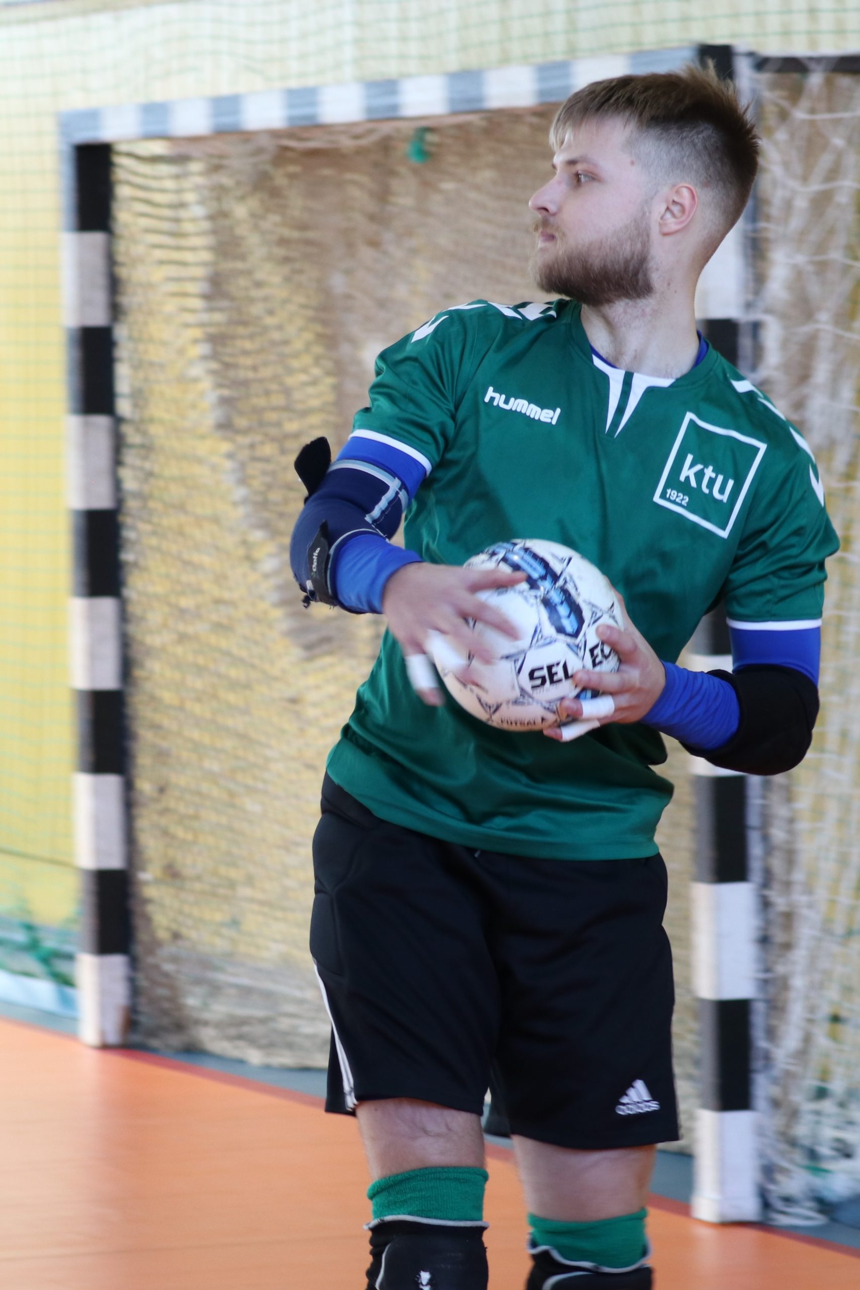 Studentas žaliais marškinėliais su KTU logotipu rankose laiko futbolo kamuolį