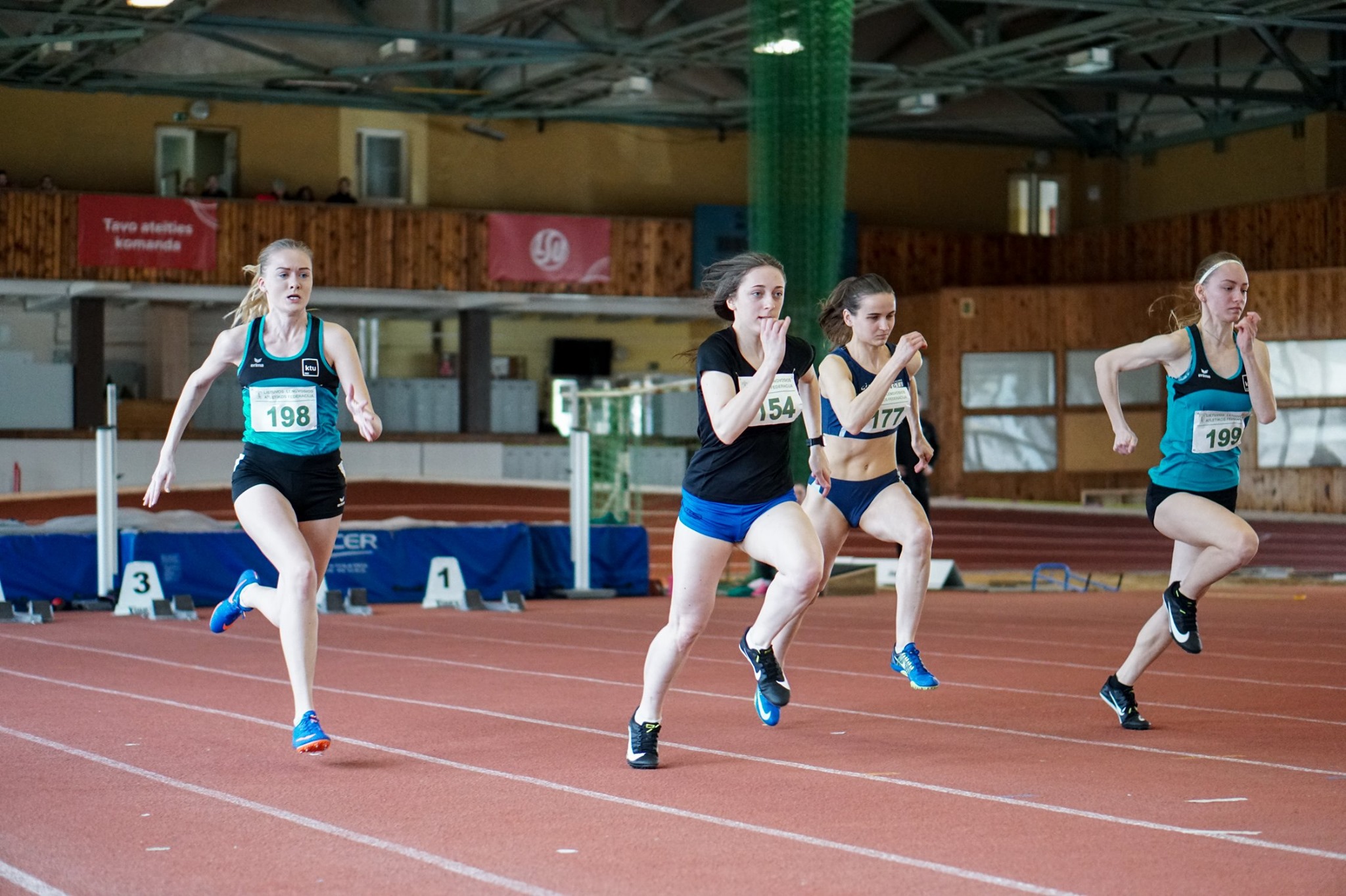 Lengvosios atletikos maniežo bėgimo takelyje bėga keturios merginos 