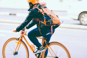 Žmogus su šalmu važiuoja oranžiniu dviračiu