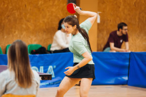 Mergina dėvinti žalsvios spalvos marškinėlius muša kamuoliuką stalo teniso rakete 